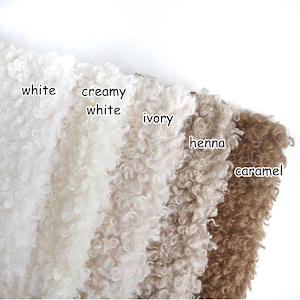 May include: Five swatches of curly, textured fabric arranged side by side. The colors are labeled as white, creamy white, ivory, henna, and caramel. Each section displays a dense, looped pile surface with a consistent, uniform appearance.