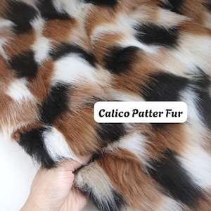 May include: A piece of faux fur fabric featuring a calico pattern with patches of white, black, and brown. The texture is long and soft, with a visible white label overlaying the fabric that reads Calico Patter Fur in black text.
