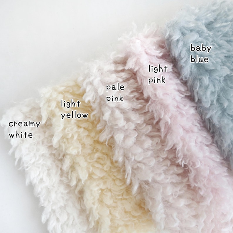 May include: Close-up of soft, textured fabric samples in creamy white, light yellow, pale pink, light pink, and baby blue. Each sample is labeled with its color name. The fabric has a fluffy, curly appearance.