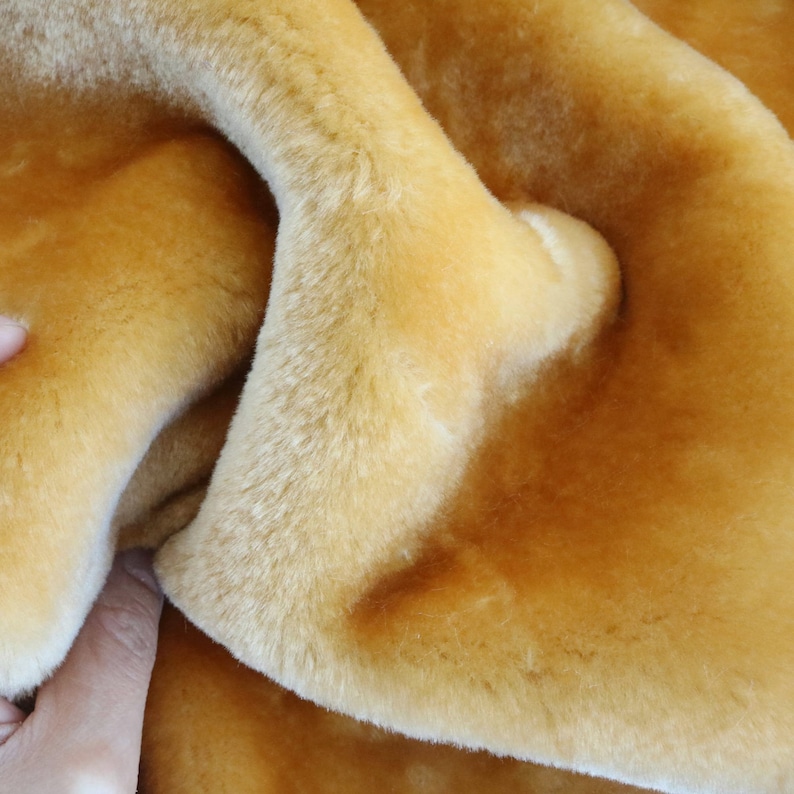 May include: A close-up of a soft, golden brown faux fur fabric. The fabric is folded and textured, showing the plush pile.