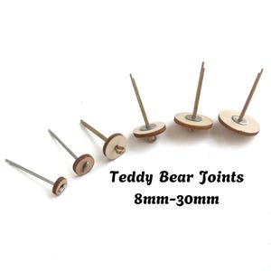 May include: Five teddy bear joints of varying sizes, each featuring a circular wooden disc, a metal washer, and a long metal pin with a loop at the end. The text "Teddy Bear Joints 8mm-30mm" is printed in black in the center of the image.