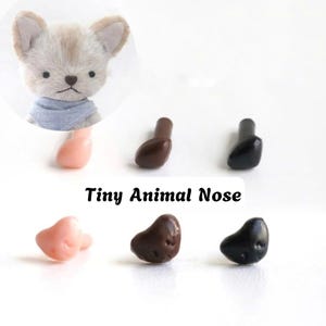 May include: A collection of small, smooth animal noses in pink, brown, and black, featuring a post for attachment. The text Tiny Animal Nose is displayed above the items, accompanied by an illustration of a small, furry animal wearing a blue scarf.