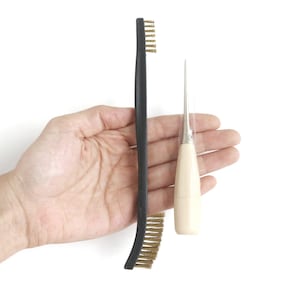 May include: A black handled tool with a brass bristle brush and a wooden handled awl with a metal needle.