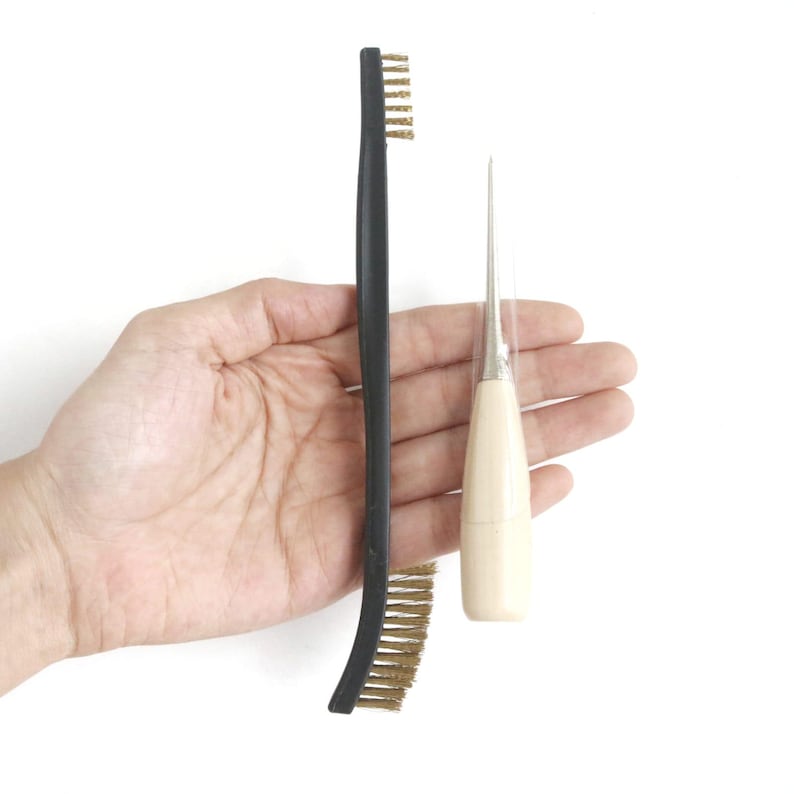 May include: A black handled tool with a brass bristle brush and a wooden handled awl with a metal needle.