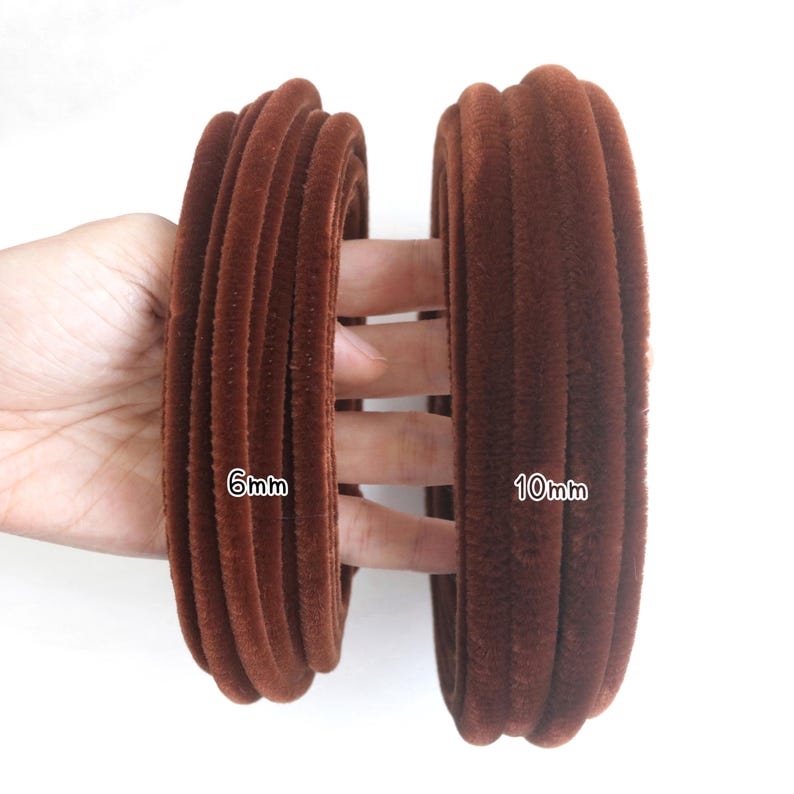 May include: Two coils of brown velvet piping trim, one labeled 6mm and the other labeled 10mm. The trim has a soft, fuzzy texture and a rounded, corded profile. The coils are displayed side-by-side to show the difference in thickness.