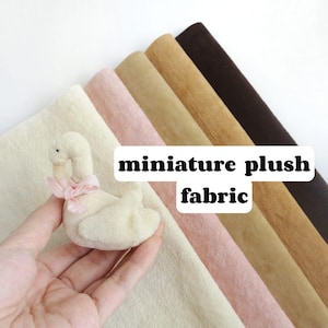 May include: A miniature plush swan with a pink bow is held in front of a cream-colored fabric. Behind it are rolls of plush fabric in shades of pink, tan, and brown. The text "miniature plush fabric" is displayed.