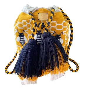 May include: A handmade yellow crochet bucket bag with a honeycomb and bee pattern. The bag features navy blue tassels and a drawstring closure. The strap is a twisted cord in yellow and navy blue. A small leather tag is attached to the bag.