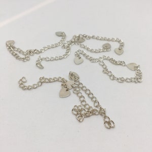 Peut inclure: Un collier en chaîne argent avec plusieurs breloques en forme de cœur. La chaîne est délicate et a un design simple.