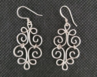 May include: A pair of silver earrings with a delicate, intricate design. The earrings are made of wire that is twisted and curled into a floral pattern.