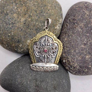 May include: Silver and gold pendant with a red stone in the center. The pendant features a stylized design with intricate details.