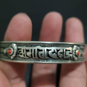 May include: Silver bracelet with Tibetan script and two red coral accents.