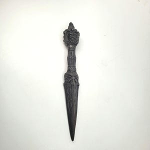 May include: A dark gray decorative dagger with an ornate handle featuring a detailed face and floral designs. The blade is long and pointed. The dagger is approximately 10 inches long.