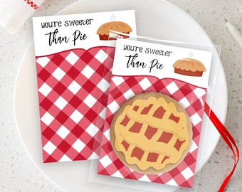 May include: Two red and white gingham patterned cards with the text "You're Sweeter Than Pie" and a cartoon pie illustration. A clear cellophane bag with a red ribbon contains a cookie shaped like a pie.