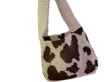 May include: A white crocheted tote bag with a brown and white cow print design. The bag has a single strap.