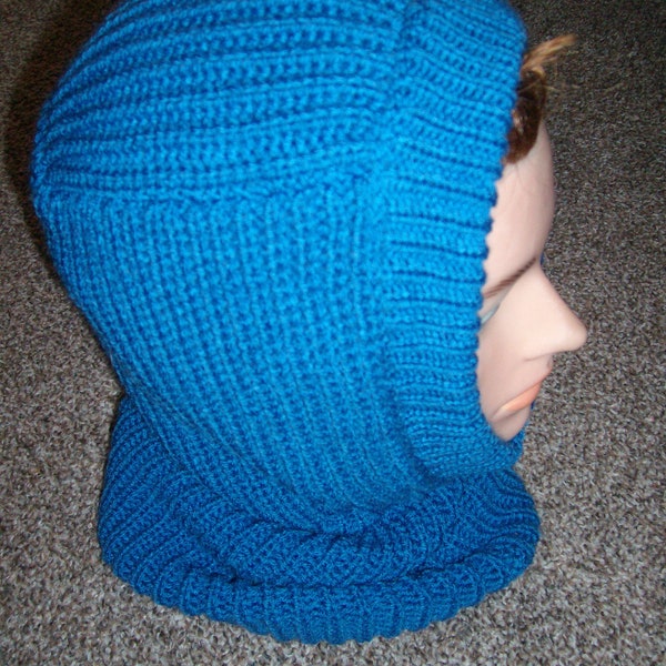 Puede incluir: Una capucha de punto en color azul cerceta brillante con textura acanalada que cubre la cabeza y se extiende hasta un cuello tipo bufanda. La prenda presenta un patrón de punto vertical consistente en toda la pieza, ofreciendo un aspecto uniforme.