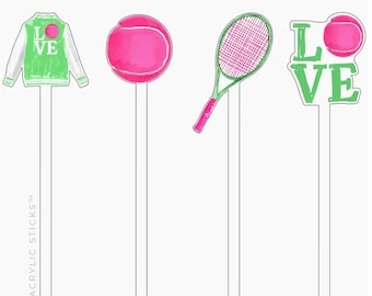 May include: Four acrylic drink stirrers with different designs. The first stirrer has a green and white varsity jacket with the word "LOVE" on the front. The second stirrer has a pink tennis ball. The third stirrer has a pink and green tennis racket. The fourth stirrer has the word "LOVE" in green letters.