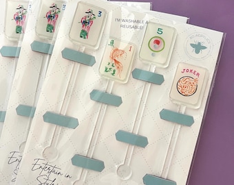 May include: A set of four clear acrylic stir sticks featuring Mahjong tile designs, including a 3, a 1 with a fish, a 5, and a Joker. The packaging includes the text "I'M WASHABLE & REUSABLE!", "Entertain in Style", and "4 PACK OF 6.25" ACRYLIC STIR STICKS".