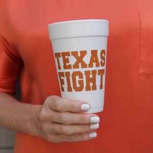 Może przedstawiać: Biały kubek z pianki z nadrukiem "TEXAS FIGHT" w pomarańczowych literach.