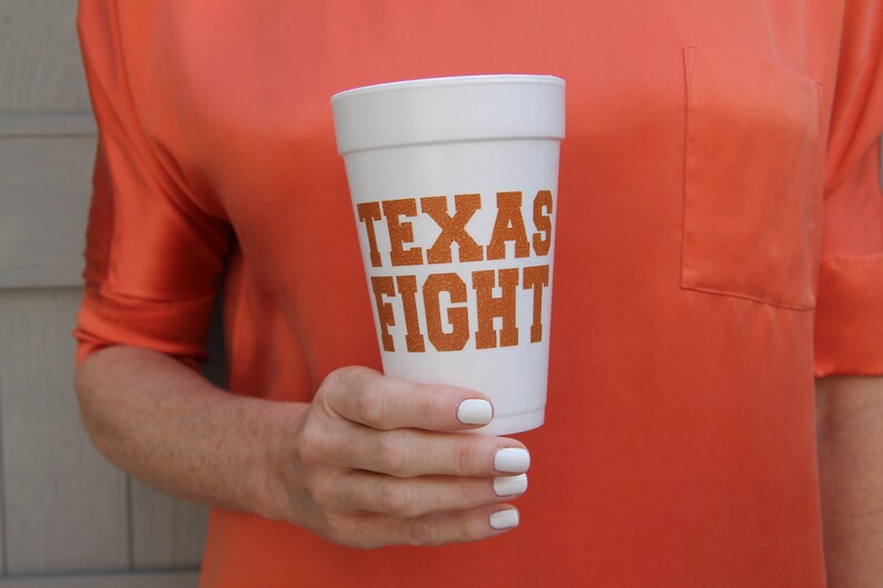 Może przedstawiać: Biały kubek z pianki z nadrukiem "TEXAS FIGHT" w pomarańczowych literach.