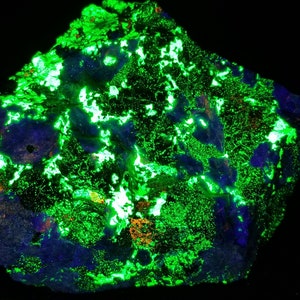 May include: A dark, rough rock with a green and blue fluorescent glow. The rock is covered in small, bright green crystals that are visible under UV light.