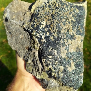 May include: A large, rough, grey rock with a large patch of dark green, sparkly mineral embedded in it.