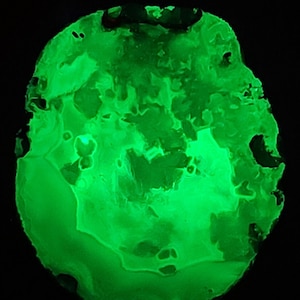 May include: A glowing, irregularly shaped object with a vibrant green hue against a black background. The surface has a textured appearance with various patterns and small holes, creating a unique, organic aesthetic. The object appears to be illuminated from within.