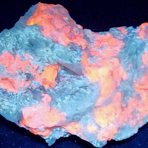 May include: A close-up of a rock formation with a fluorescent orange and gray color scheme. The rock has a rough texture and irregular shape. The letters "LW" are in the upper left corner.