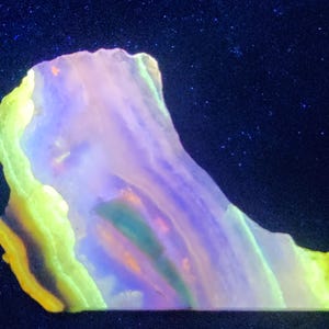 May include: A polished slab of mineral showing vibrant fluorescence under ultraviolet light. The specimen displays distinct bands of neon yellow, bright purple, and deep blue, with a translucent, layered structure and irregular, jagged edges.