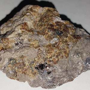 Könnte beinhalten: Ein rauer, grauer Stein mit Flecken aus goldenen und braunen Mineralablagerungen.