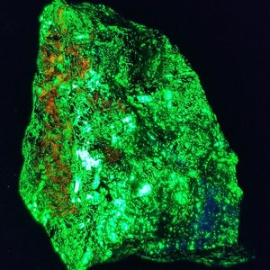 Könnte beinhalten: Ein großer, dunkelgrüner Stein mit einer rauen, strukturierten Oberfläche. Der Stein leuchtet unter Schwarzlicht hellgrün.