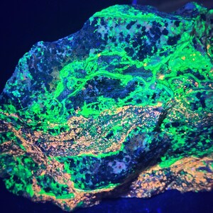 May include: A close-up of a rock formation with vibrant colors. The rock displays a mix of neon green, blue, and orange hues. The texture appears rough and uneven, with a dark background.