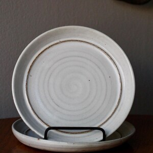 May include: Two white ceramic plates with a brown rim and a concentric circle design. The plates are stacked on top of each other.