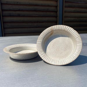 May include: Two white ceramic bowls with a textured rim. The bowls are speckled with brown flecks and have a slightly off-white color.
