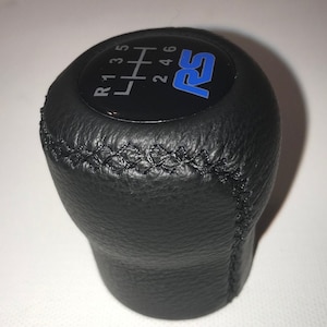 May include: Black leather gear shift knob with a black and blue circular emblem that says "RS" and a black and white gear shift pattern that says "R 1 3 5  2 4 6".