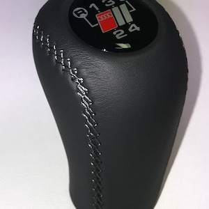 May include: Black leather gear shift knob with a black and silver gear shift pattern and the Audi logo. The gear shift pattern shows the letters R, 1, 3, 5, and the numbers 2 and 4.