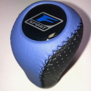 May include: Blue and black leather gear shift knob with a black and silver "SPORT" logo with a blue "F" inside.
