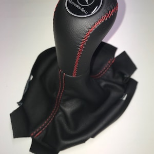 May include: Black leather gear shift knob with red stitching and a silver Mercedes-Benz logo.