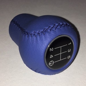 Könnte beinhalten: Blauer Lederschaltknauf mit schwarzem Schaltmuster und weißen Zahlen 1, 2, 3, 4, 5 und R.