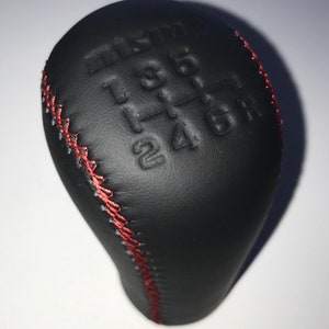 May include: Black leather gear shift knob with red stitching and a 6-speed pattern embossed on the top.