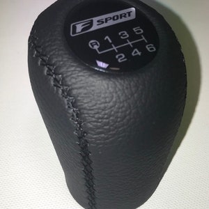 May include: Black leather gear shift knob with white stitching and a black circular plate with the text "F SPORT" and a 6-speed gear pattern.