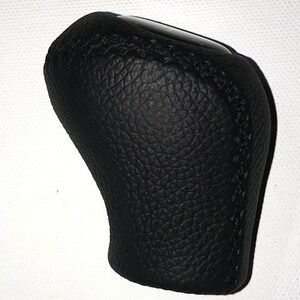May include: Black leather gear shift knob with a textured surface and stitched seams.