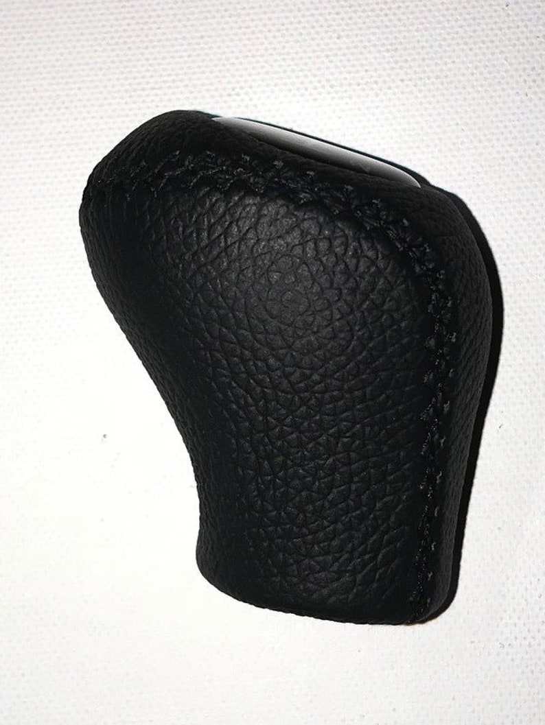May include: Black leather gear shift knob with a textured surface and stitched seams.