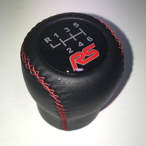 May include: Black leather gear shift knob with red stitching and a silver gear pattern with the letters "RS" in red.