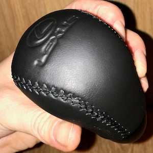 Op de afbeelding: Zwarte leren versnellingspookknop met het woord "Lexus" erop gegraveerd.