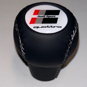 May include: Black leather gear shift knob with white stitching and a white, red and black Audi Sport quattro logo.