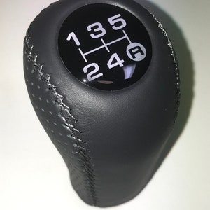 May include: Black leather gear shift knob with white stitching and a black gear shift pattern with white numbers 1, 2, 3, 4, 5 and R.