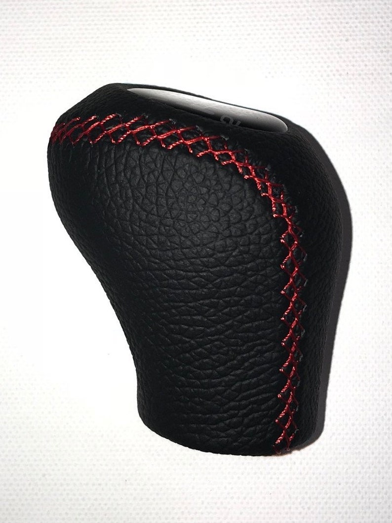 May include: Black leather gear shift knob with red stitching.