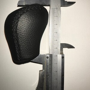 May include: A black leather gear shift knob being measured with a caliper. The caliper reads 6 cm.