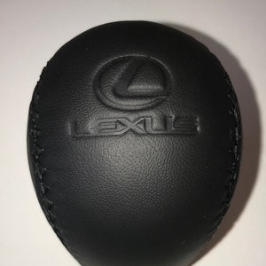 May include: Black leather car gear shift knob with a stitched edge and the Lexus logo embossed on the top.