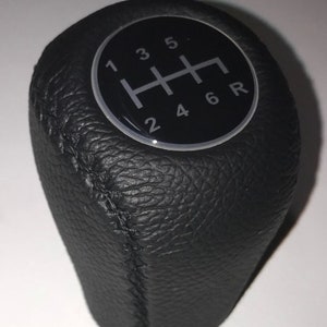 May include: Black leather gear shift knob with a silver and black gear pattern. The pattern shows the numbers 1, 2, 3, 4, 5, 6, and R.